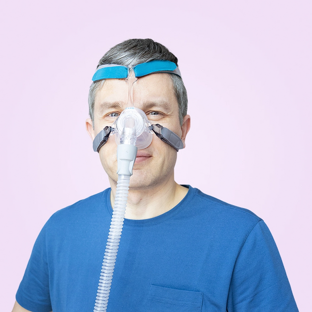 Man wearing a blue Löwenstein Cara Nasal CPAP Mask on a pink background