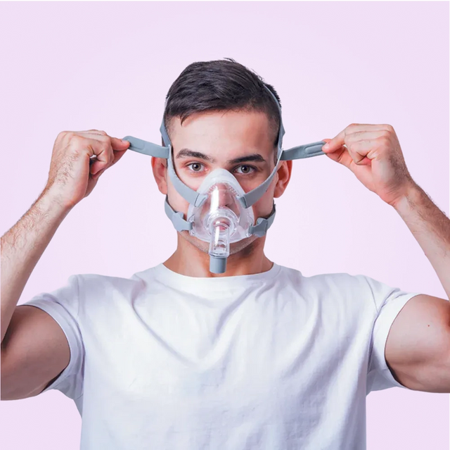 Person adjusting his BMC F5A Full Face CPAP Mask against a pink background