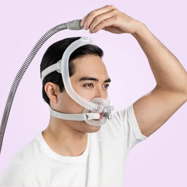 Person wearing a ResMed AirFit™ F30i Full Face Mask with a hose on a pink background