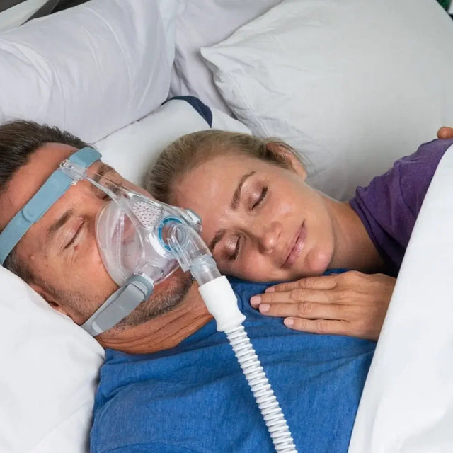 Man wearing a Fisher & Paykel Vitera Full Face CPAP Mask, lying in bed with a woman