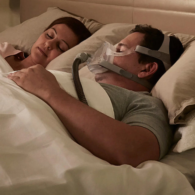 Man wearing a ResMed AirFit™ F10 Full Face Mask while sleeping next to a woman in bed.