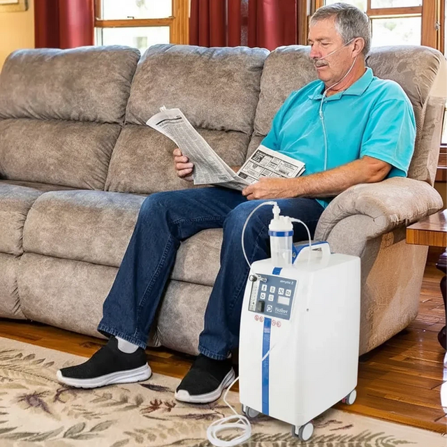 Man sitting on a couch with a KROBER AEROPLUS E 5l/min Oxygen Concentrator next to him
