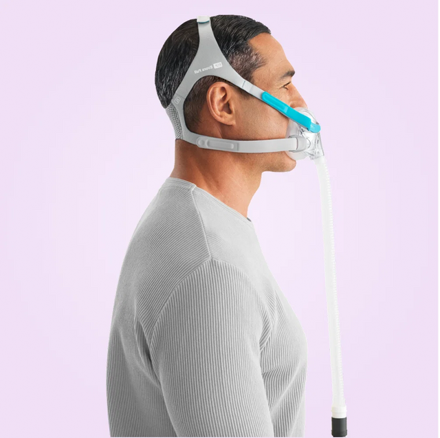 Person wearing a Fisher & Paykel Evora Full Face CPAP Mask with a hose on a light purple background side view