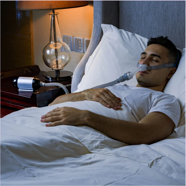 Man using a BMC P2H Nasal Pillow CPAP Mask in bed with a nightstand lamp in the background