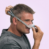 Man adjusting a Fisher & Paykel Brevida Nasal Pillows CPAP Mask on a light purple background