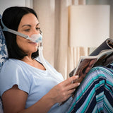 Woman wearing a Fisher & Paykel Brevida Nasal Pillows CPAP Mask while reading a magazine in bed.
