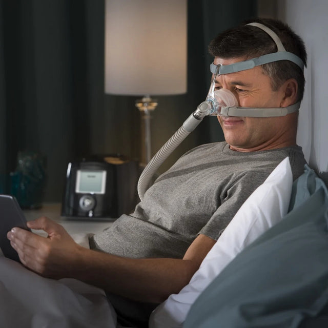 Man using a CPAP machine with a Fisher & Paykel Eson 2 Nasal CPAP Mask in bed with a dark room setting