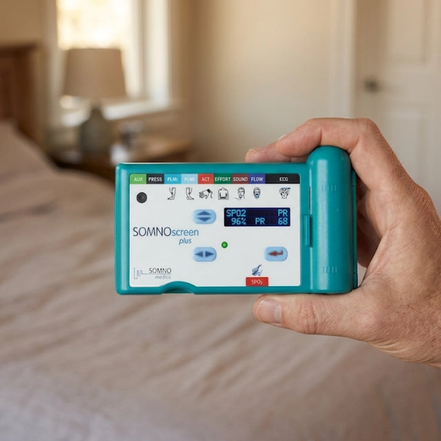 Hand holding SOMNOscreen™ Plus polysomnography (PSG) system in a bedroom setting