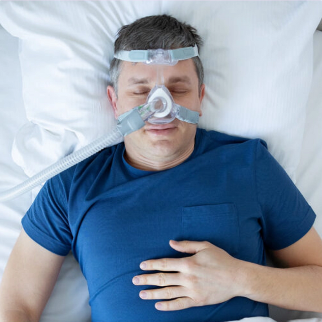 Man lying in bed wearing a Löwenstein JOYCEone Nasal CPAP Mask, with a blue shirt.