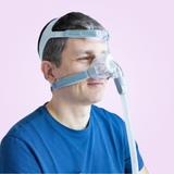 Man wearing a Löwenstein JOYCEone Nasal CPAP Mask with a clear hose on a pink background