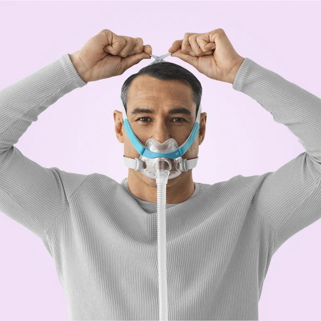 Person adjusting a Fisher & Paykel Evora Full Face CPAP Mask with a light purple background