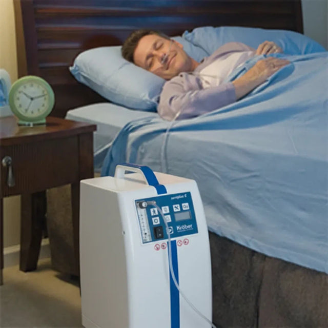 Man sleeping in bed with a KROBER AEROPLUS E 5l/min Oxygen Concentrator next to him on the floor