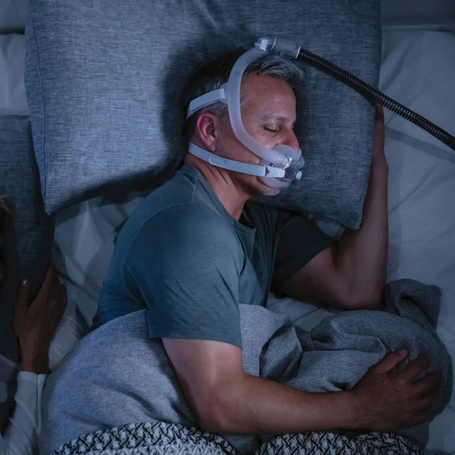 Man wearing a ResMed AirFit™ F30i Full Face Mask in bed, using a CPAP machine.