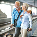 Senior couple walking together with suitcases in an airport terminal while the man is using Inogen Rove 6 Portable Oxygen Concentrator