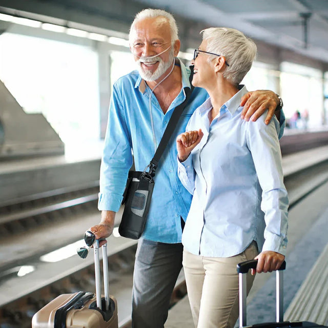 Senior couple walking together with suitcases in an airport terminal while the man is using Inogen Rove 6 Portable Oxygen Concentrator