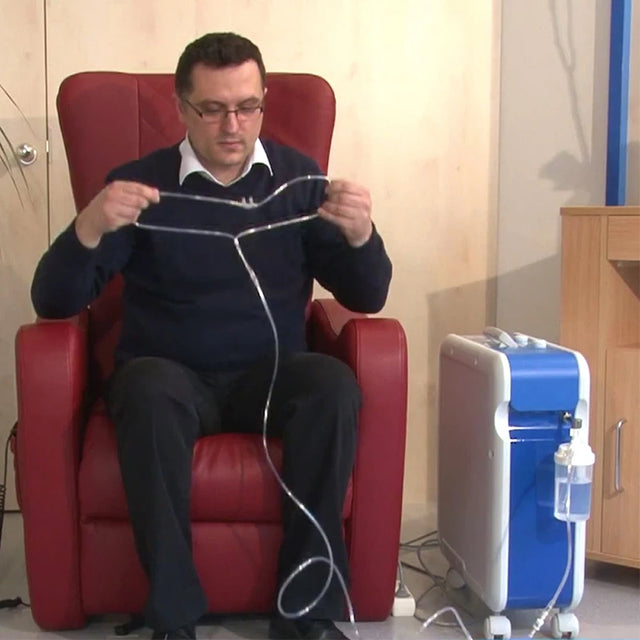 Man sitting in a red chair holding a black sweater with white stripes, with a Kröber O2 Oxygen Concentrator