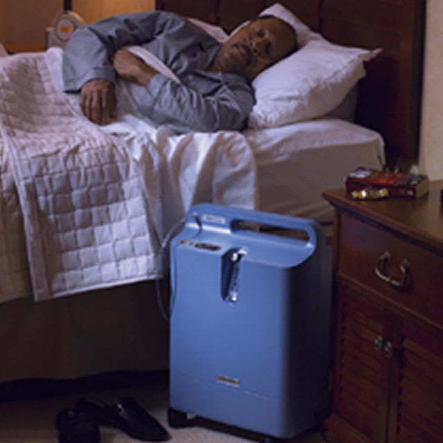 Person lying in bed with a Philips EverFlo Home Oxygen System concentrator next to them