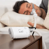 Man sleeping with ResMed Airmini Auto Travel CPAP machine on his nightstand.