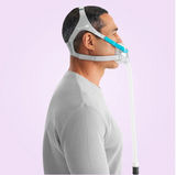 Person wearing a Fisher & Paykel Evora Full Face CPAP Mask with a hose on a light purple background side view