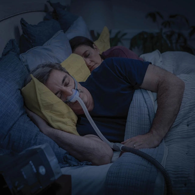 Two people lying in bed with one using a ResMed AirFit N30 Nasal CPAP Mask