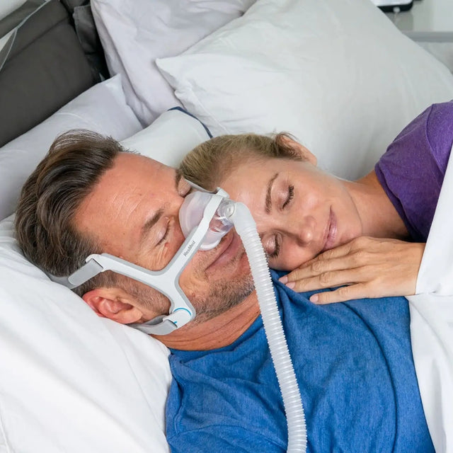 Man wearing a ResMed AirTouch N20 Nasal CPAP Mask with a woman lying next to him in bed