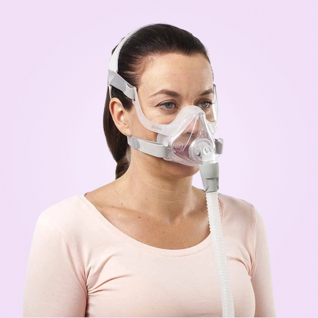Woman wearing a ResMed AirFit™ F10 For Her Full Face Mask against a light purple background