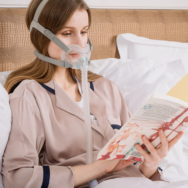 Woman using a BMC F6 Full Face CPAP Mask while reading a book in bed