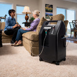 Two people sitting on a couch in a living room with a DeVilbiss 525 Oxygen Concentrator next to them.